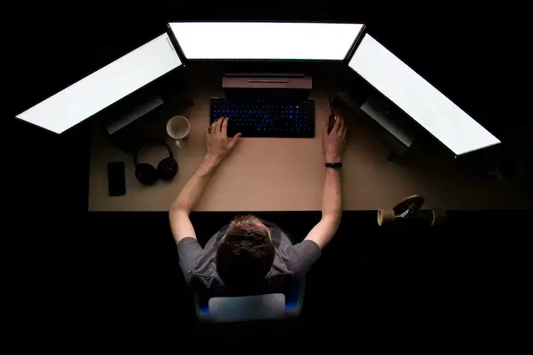 Man facing three computer monitors while sitting