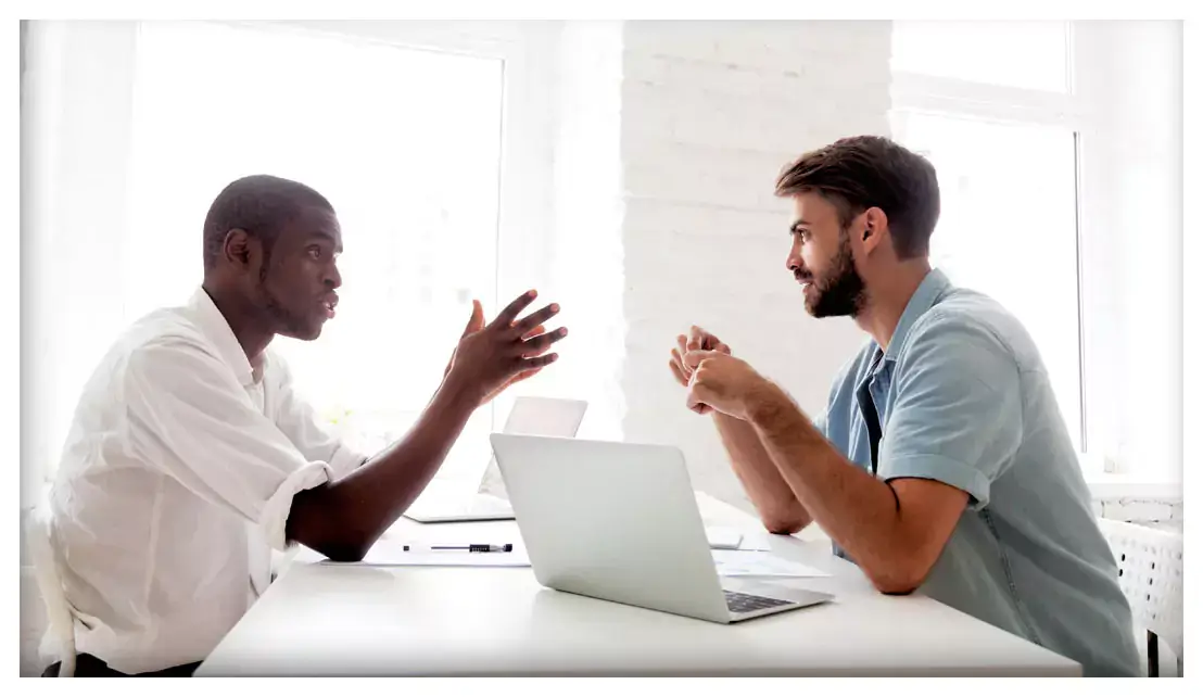 Two people having a discussion at a table with a laptop on it