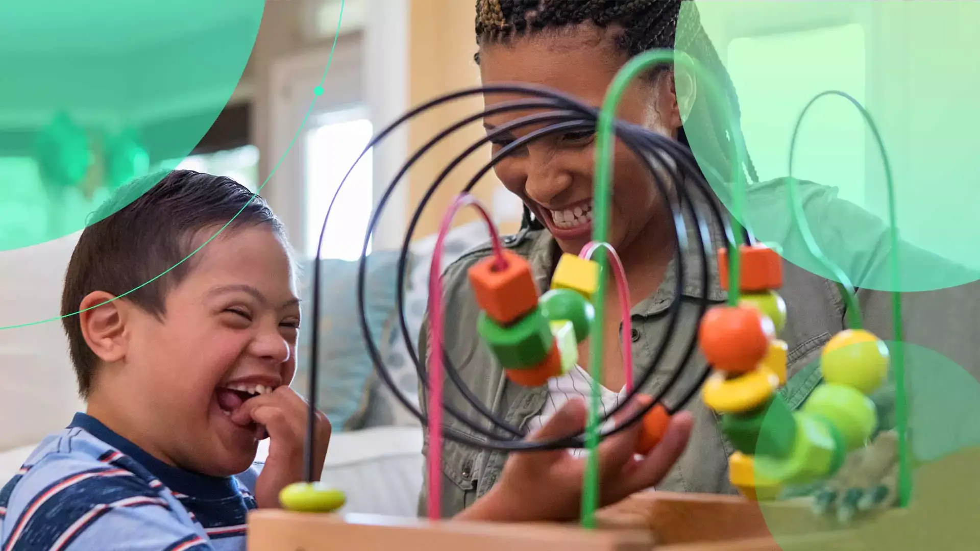 A young boy smiling and playing with a toy with a special care counsellor by his side